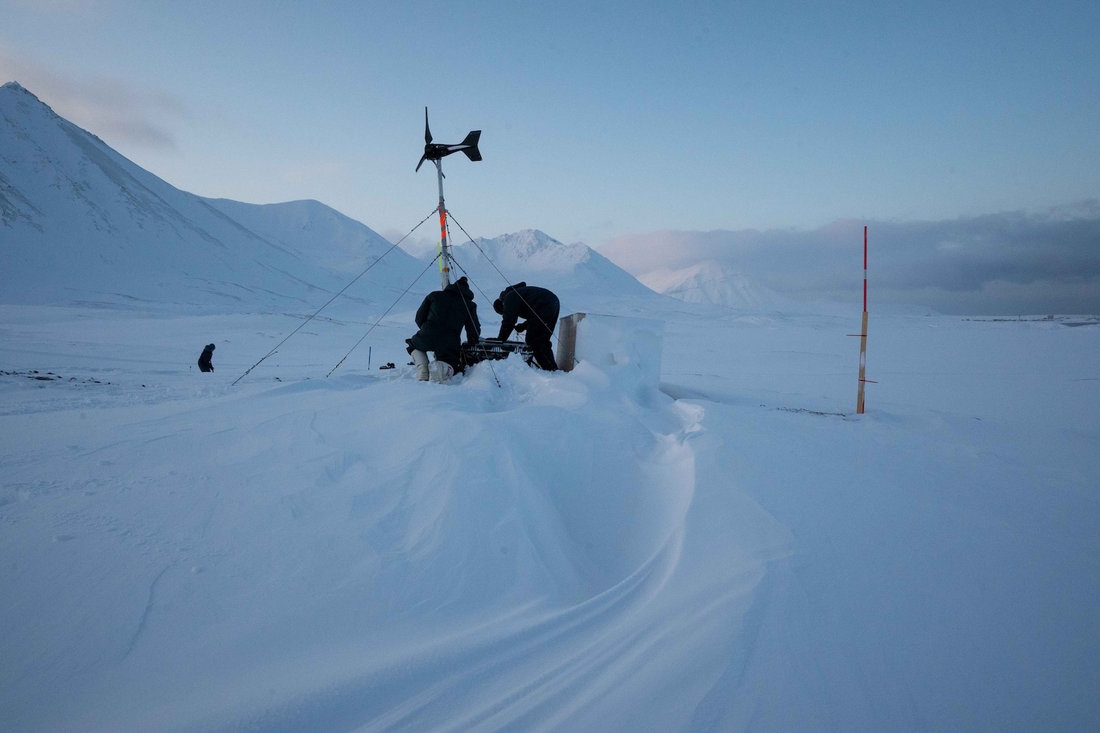 two researchers kneel in the snow adjusting equipment